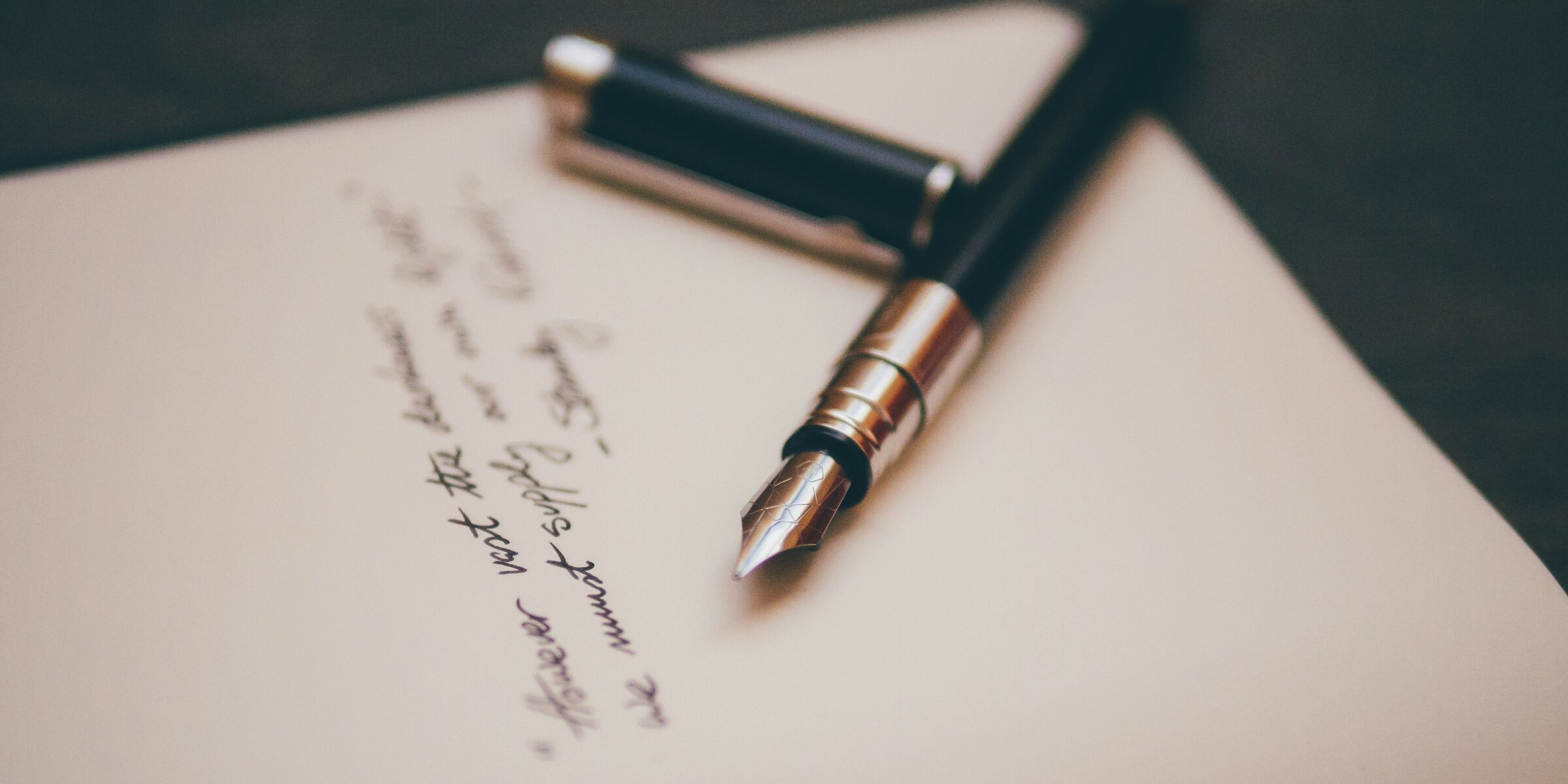 A black and silver fountain pen resting on a sheet of paper covered in handwritten cursive