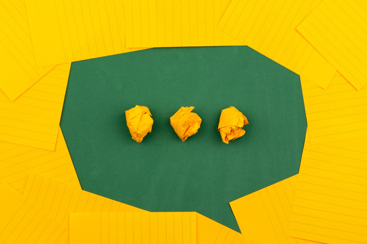 Three crumpled yellow papers on green surface surrounded by yellow lined papers