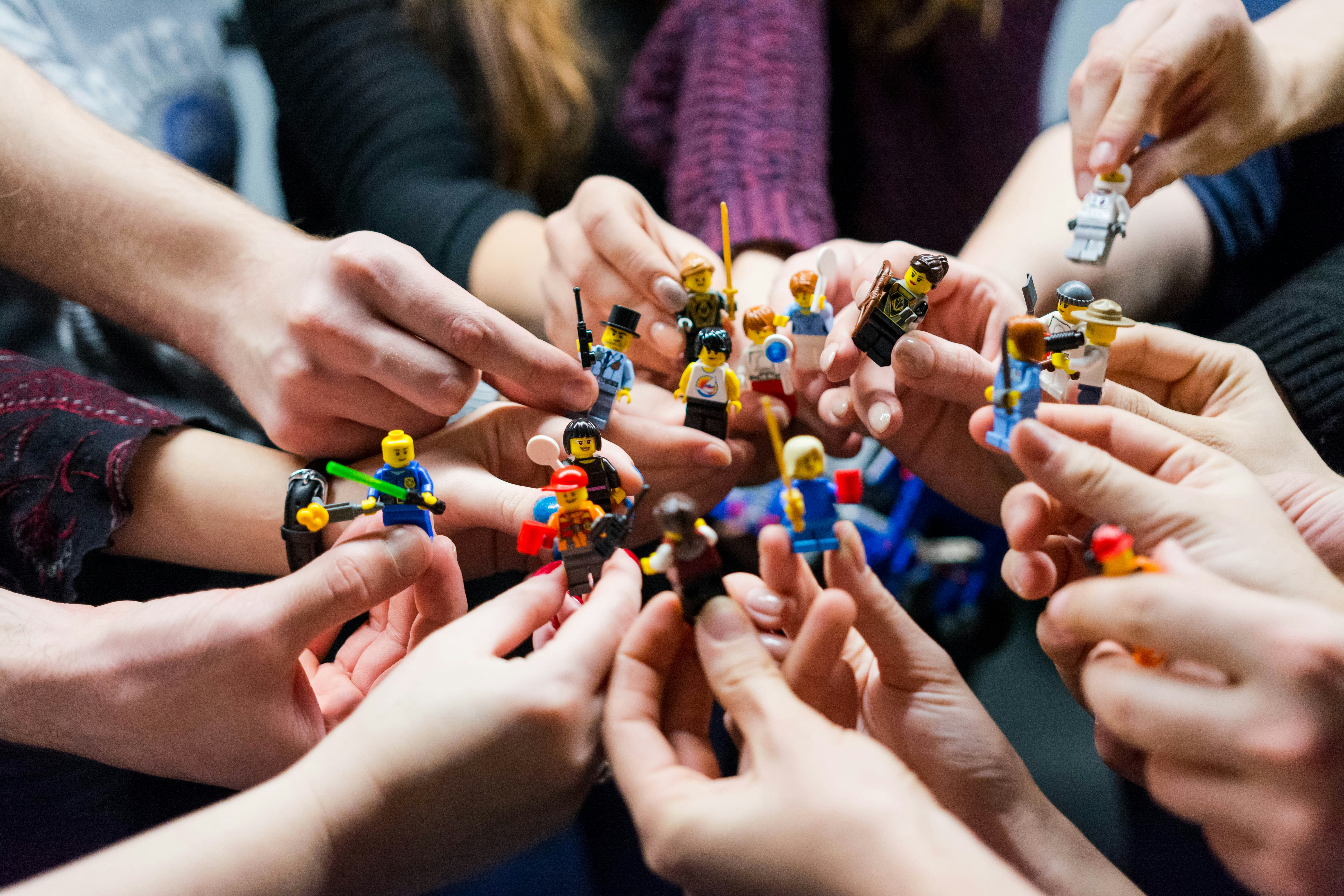 A circle of many hands each holding a small toy figure, representing a team coming together