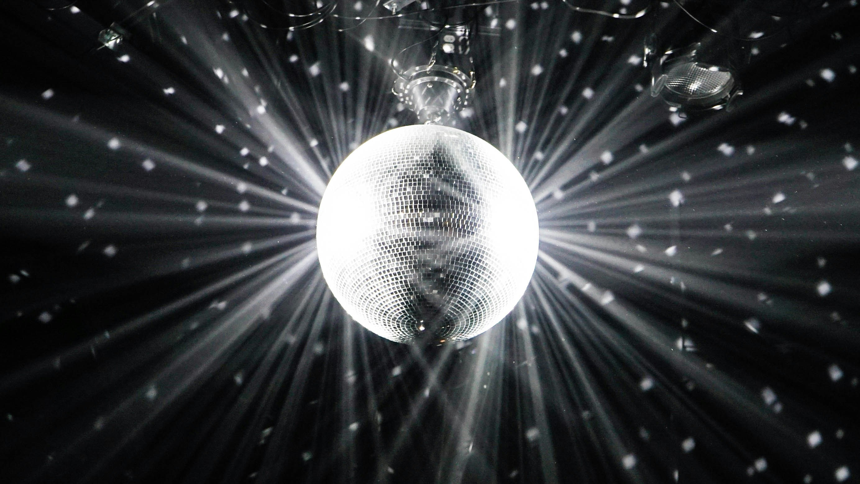 A glowing mirror ball in a dark room, throwing beams and spots of white light in every direction