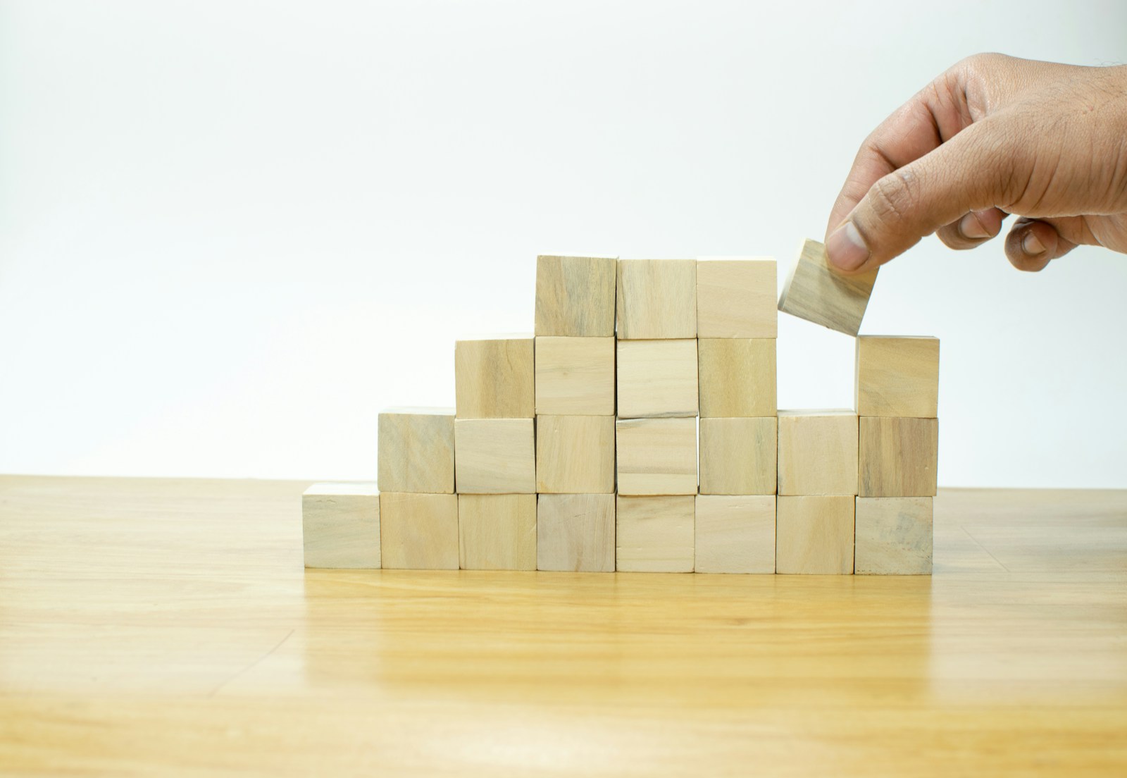 A person placing a block onto a pile of wooden blocks