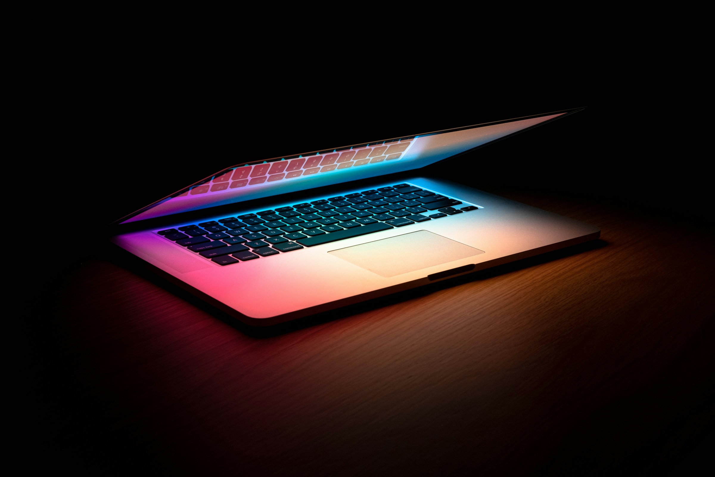 Partly open MacBook Pro on a wooden table, lit with blue, pink and orange light