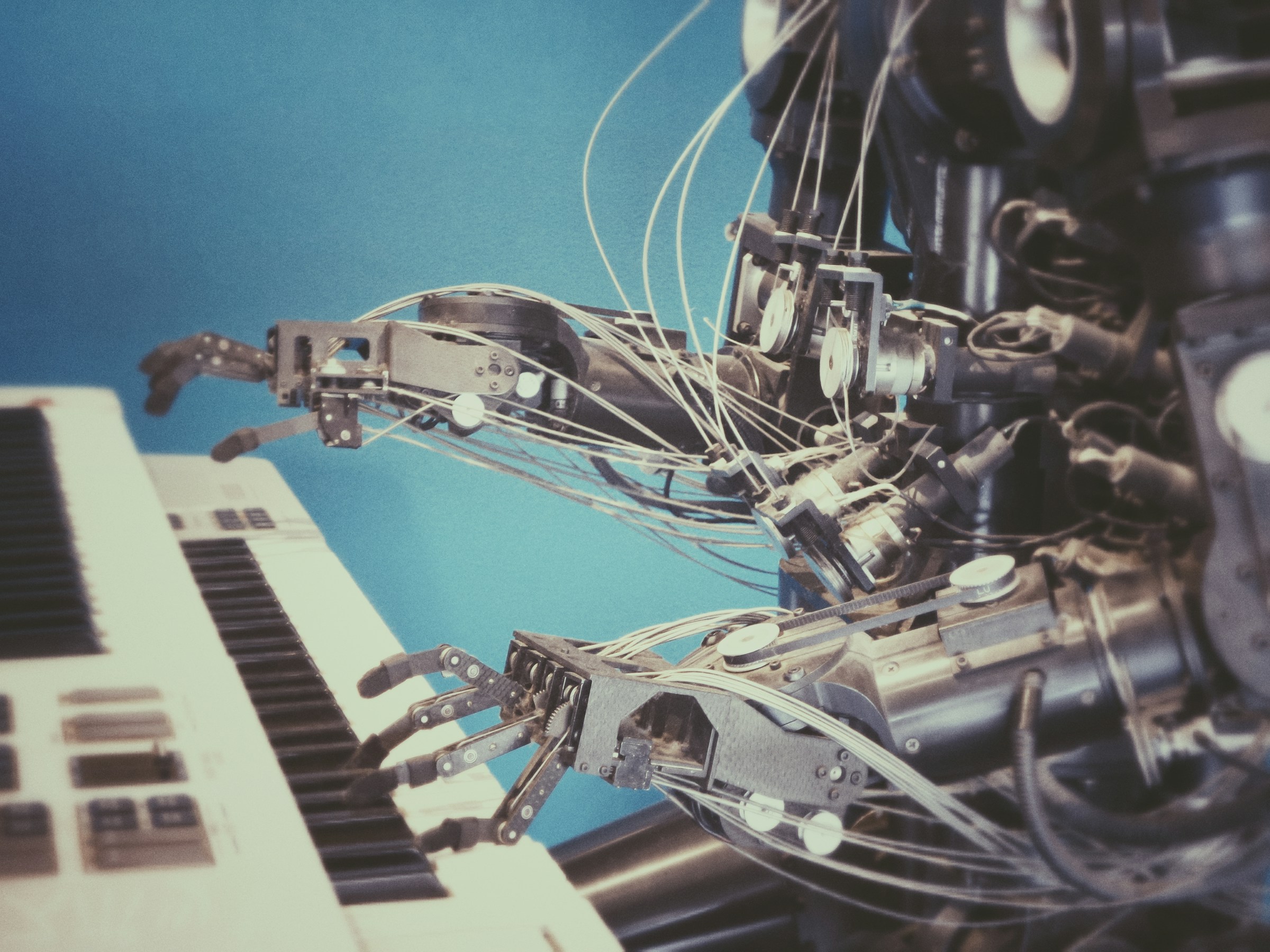 A robot with exposed cables and mechanical hands playing a keyboard against a blue background